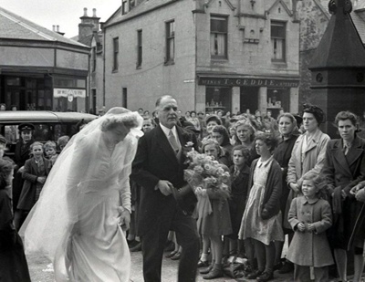 fht.2026.115  wedding at forres high church in the 1950's, with thomas geddie's grocer, wine and sprit dealer shop in the background at no 44 high street.