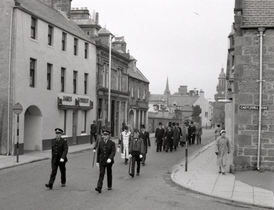 fht.2026.91  kirkin the council in 1957, passing forrest's bakers at 139 high street, (operated from 1919 to 1978).  next is the forres gazette, reid's chemist, then kelbourne fish restaurant.