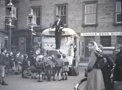 fht.2026.93  magic bus entertaining schoolchildren in 1953 outside the tolbooth, in front of thompson's the grocers at no 82 and fraser's the butchers at no 86.