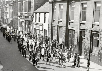fht.2026.98  parade of boys' brigade passing austin's bakers at  no 61 high street, and national bank of scotland at  no 57, circa 1960.