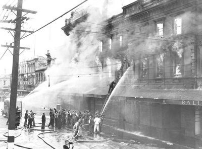Ballantyne's Fire. Central City. Firemen up Ladder. Note use of Civilians to Help Manage Hoses as well as a Sailor in the Foreground. Also Note the Traffic Lights with black and white striped Pole on Left , Colombo Street. Christchurch, Canterbury. New Zealand. 3 image item