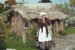 Vicki Blythe-Pope in costume, holding a broom and a bucket in front of the sod cottage in the Howick Historical Village. ; La Roche, Alan; 2010; P2020.50.24