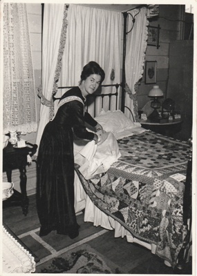 Eileen Martensen making a bed at the 1962 exhibition of the Howick Historical Society in the Howick Town Hall.; N.Z.Herald; 1962; P2022.10.13