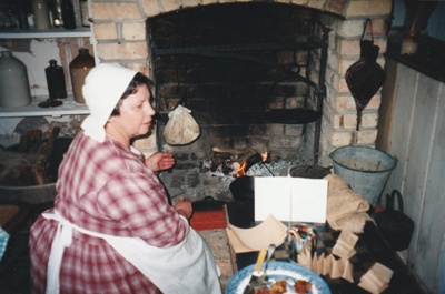 Brenda Scott (nee White) in costume, tending the fire in White's Store.; P2020.76.02