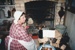 Brenda Scott (nee White) in costume, tending the fire in White's Store.; P2020.76.02