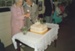 Ren Wiseman and Dorothy Beavis cutting the cake at the 25th anniversary of the Howick Historical Society. Graeme McDonald and society members are watching.; La Roche, Alan; 29 March1987; P2022.25.21