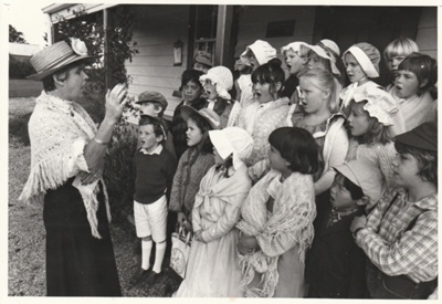 A school group,all in costume, singing outside Brindle Cottage in the Howick Historical Village. image item