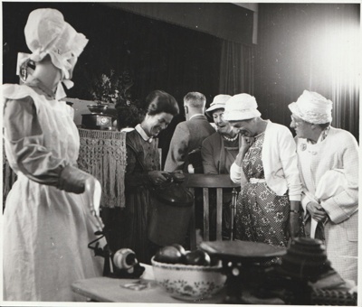 Eileen Martensen talking to visitors in a kitchen exhibit with  a mannequin at the 1962 exhibition of the Howick Historical Society in the Howick Town Hall.; Auckland Star; 1962; P2022.10.06