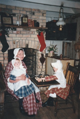 Brenda Scott, in costume, with children in front of the fireplace inWhite's Store, decoated for Christmas.; P2021.105.12