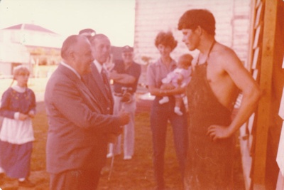 Alan Clarke presenting a poker to PM Robert Muldoon  outside Wagstaff's Forge in Howick Historical Village. ; La Roche, Alan, Howick; 29 March 1981; P2020.157.01