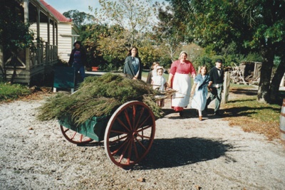 A family in costume behind a cart filled with fascines. A fascine is a rough bundle of brushwood or other material used for strengthening an earthen structure, or making a path across uneven or wet terrain. Typical uses are protecting the banks of streams from erosion, covering marshy ground and so on.; La Roche, Alan; P2022.01.16