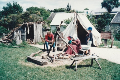 A man, woman and two children in costume, outside the tent by their fireplace on the green at Howick Historical Village.; La Roche, Alan; October 1996; P2021.88.14