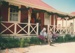 Christmas, past and present at Howick Historical Village, 12 December 1987. A lady on the veranda and two girls on the steps of De Quincey's cottage with decorations.; 12 December 1987; P2021.192.07