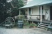 The verandah of Fitzpatrick's Cottage at Howick Historical Village, showing household items, steps, barrel and dray wheels.; La Roche, Alan; P2021.81.08