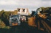 A Mack Truck towing heavy vehicle following a bulldozer clearing the way for moving half of Puhinui to its new site in the Howick Historical Village. A Johnson's truck carrying the building is in the rear.; Smith, Malcolm; May 2002; P2020.16.06