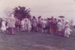 A school group with guides, all in costume, lined up on the green in Howick Historical Village.; 1982; P2021.181.03