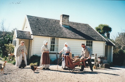 Richard Lees carting bricks outside  Briody-McDaniel Cottage. Prue Lees and two other women are also there. All are in costume. 
; La Roche, Alan; c2000; P2020.104.06