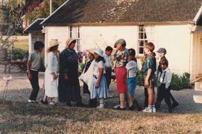 Maggie Thomson with a group of children outside Briody-McDaniel's Cottage at Howick Historical Village.

; La Roche, Alan; 1993; P2020.104.01