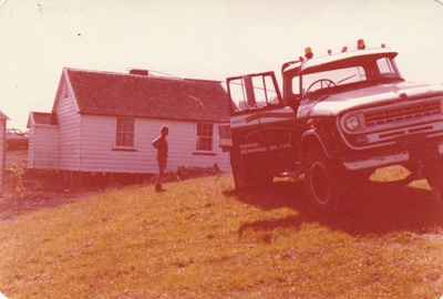 The  transporter driving away from McDermott's Cottage at Howick Historical Village on its new site.

; La Roche, Alan; 19 December 1974; P2020.100.16
