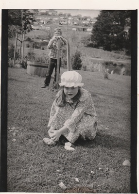 A little girl in costume sitting on the grass. behind her is a boy, standing.; Spencer, LInda, East City News; August 1983; P2021.172.03