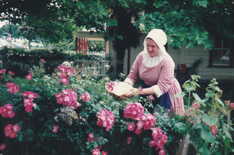 A volunteer guide in the rose garden beside Brindle Cottage in Howick Historical... eHive