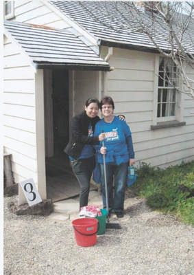 Two BNZ workers standing in front of Briody Cottage in Howick Historical Village on BNZ staff volunteer day with cleaning materials.; 4 September 2013; P2021.160.06