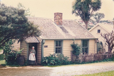 Lois Abram holding a broom at the entrance to Maher-Gallagher Cottage on Church Street at the Howick Historical Village.; La Roche, Alan; 2000; P2020.91.30