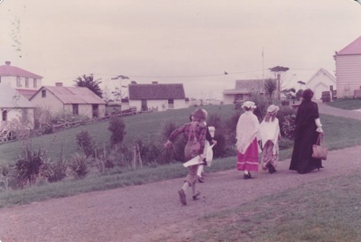 A class of schoolchildren with an adult, all in costume, walking along Grey Street at Howick Historical Village.; 1982; P2021.107.03