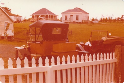 Two vintage cars in front of the Methodist Church in Howick Historical Village, looking over the green to De Quincey's and Johnson's cottages.; 16 November 1980; P2021.108.03