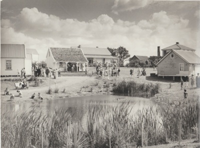 Howick Historical Village showing people, buildings and the pond in the foreground.; 8/03/1980; 2019.100.01