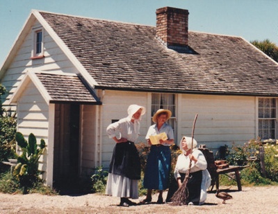 Lois Abram (with broom) and two other women in costume outside Maher-Gallagher Cottage on Church Street at the Howick Historical Village.; La Roche, Alan; P2020.92.06