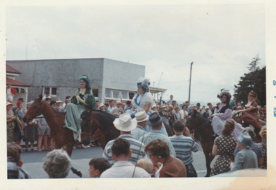 The crowd watching women riding side-saddle in costume in a horse-drawn cart in the Howick Santa Parade, 30th November 1960.; Young, Heather; 30 November 1960; P2022.06.08