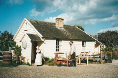 Richard Lees standing next to his brick  cart outside  Briody-McDaniel Cottage talking to a woman. Both in costume.
; La Roche, Alan; c2000; P2020.104.-5