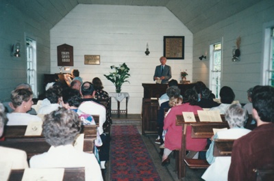Rev. Frank Ashby in the pulpit of the Howick Methodist Church ih the Howick Historical Village. Harvest Festival April1999. Muriel Ashby is playing the organ.; La Roche, Alan; P2020.37.04