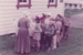 A school group with a guide, all in costume, outside  Brindle Cottage in Howick Historical Village.; 1982; P2021.181.02
