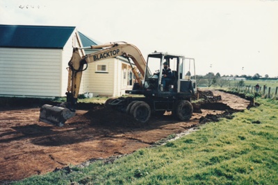 A digger preparing a road and carpark behind White's Homestead at Howick Historical Village.; La Roche, Alan; 6 November 1995; P2021/66/01