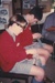 Two schoolboys learning how to darn socks in Historical Village during a school visit.; 1999; P2021.185.03