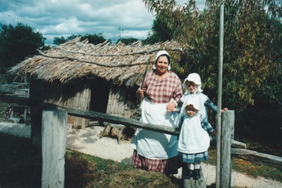 Tracy Mulgrew (left with broom) and Brenda Scott and her granddaughters (right) outside the mail runner's cottage in Howick Historical Village.; La Roche, Alan; P2021.83.07