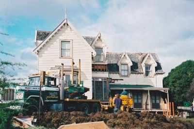 A Johnson's truck and a digger in front of Puhinui on its new site in the Howick Historical Village.; Alan La Roche; May 2002; P2020.11.46