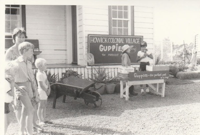 Visitors watching Philip la Roche and David Bramwell in costume, at the Guppie stall on a Live Day  in Howick Historical Village.; La Roche, Alan; 5 April 1981; P2021.129.02