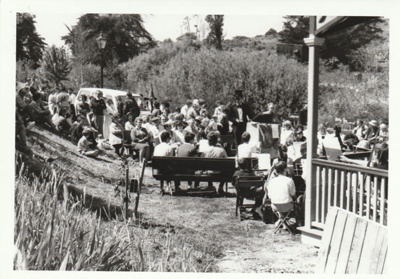 People listening to the Auckland Youth Symphonic Band outside Puhinui, on a Gala day at Howick Historical Village.; La Roche, Alan; 1986; P2021.178.09