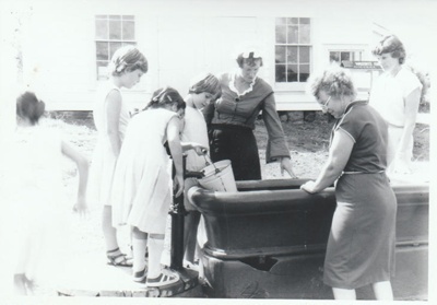 A school visit being shown how water was pumped into a bucket before washing was done; 1981; P2021.95.01