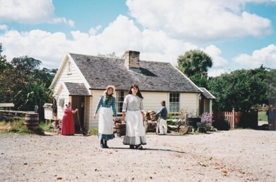 Two girls carrying a bucket of water in front of Briody-McDaniel cottage. ; 22 August 2006; 2019.196.14