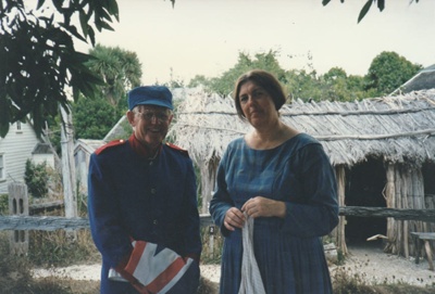 Alan la Roche in Fencible uniform and Marin Burgess (in costume) outside Hemi Pepene's raupo hut at Howick Historical Village.; La Roche, Alan; P2021.118.29