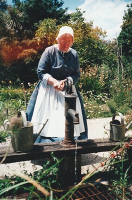 Lois Abram, in costume, at the water pump in Howick Historical Village.; P2021.105.13