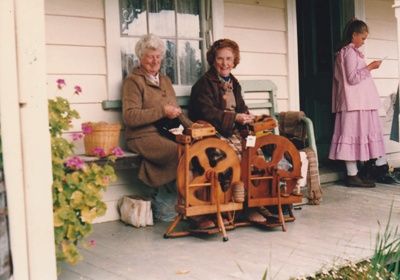 Wynn Pavitt and another guide spinning on the verandah at Sergeant Barry's cottage in Howick Historical Village. ; 1980; P2020.132.03