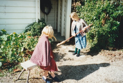 Two girls in costume,outside a cottage on a Live Day in Howick Historical Village. One is sweeping the path.; La Roche, Alan; P2021.98.10