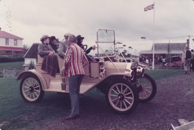 A man looking at people driving a vintage car in Howick Historical Village. Bell House and Brindle cottage are in the background.; La Roche, Alan; June 1982; P2021.108.17