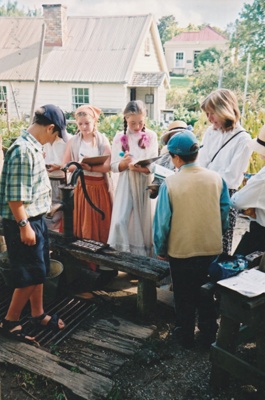 Children in costume, writing on slates with a teacher, in Howick Historical Village.; P2021.107.13