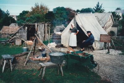 A man and woman in costume outside the tent on the green at Howick Historical Village.; La Roche, Alan; October 1996; P2021.88.13
